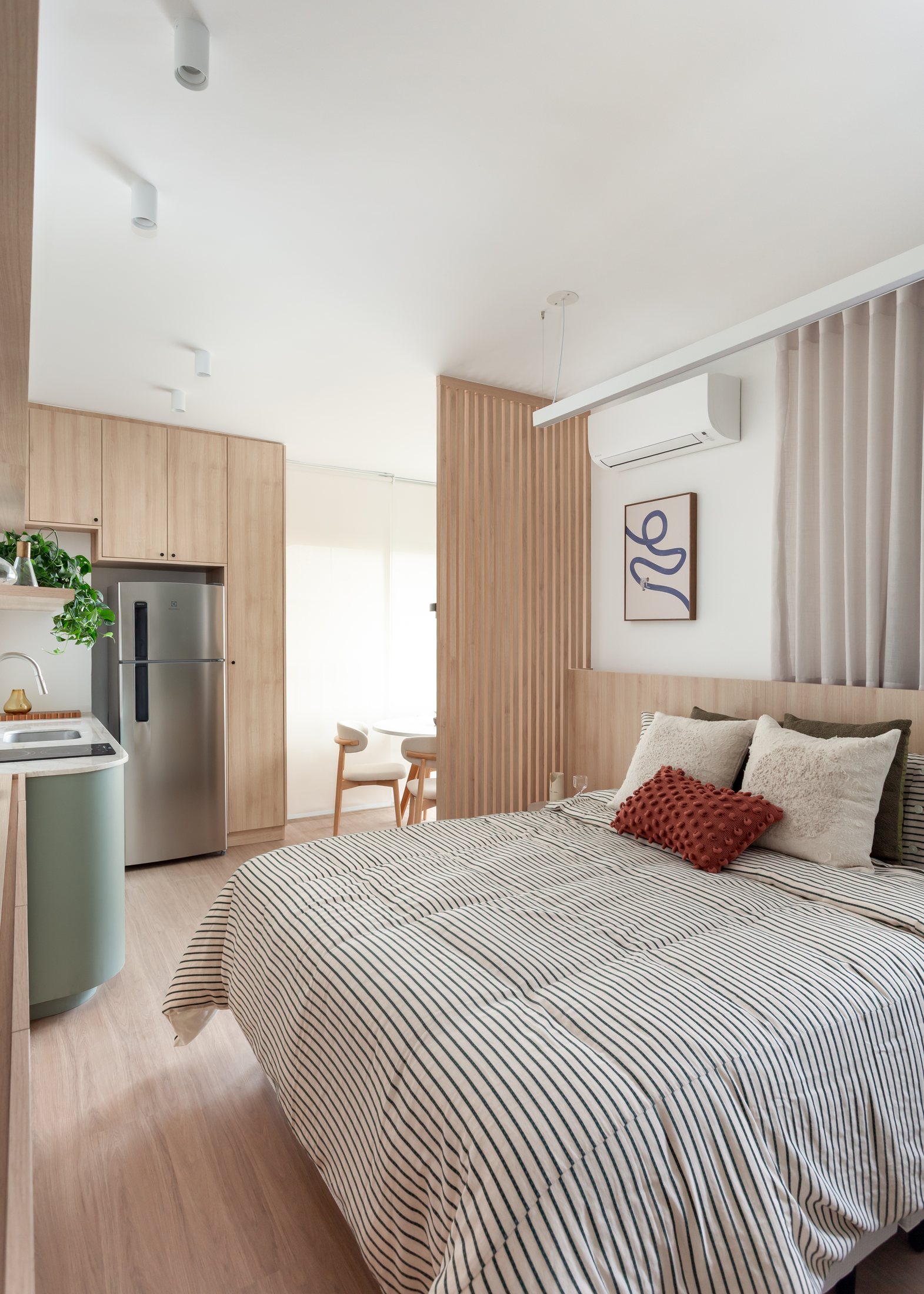 Studio Vila Mariana com cama, marcenaria clara, cozinha integrada e ripado.